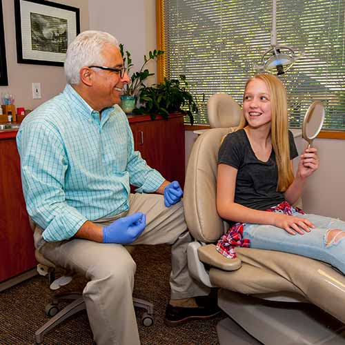 Dr. Jeff Schur meeting with a female teenage patient holding a mirror, smiling at her orthodontic results.